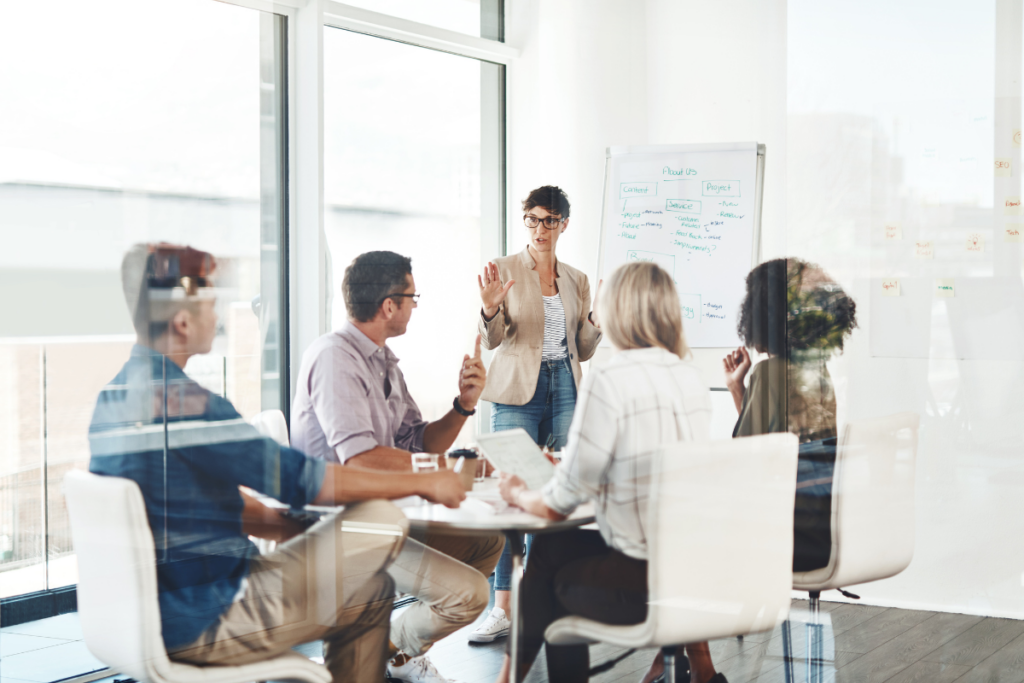group of employees in a conference room with a woman presenting at a whiteboard