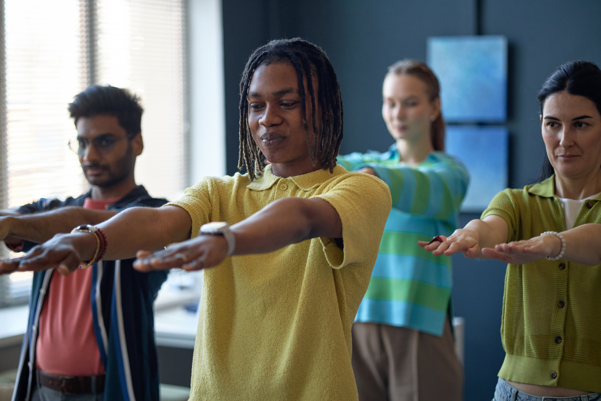 Four people in a workplace with their arms outstretched in a yoga or exercise position.
